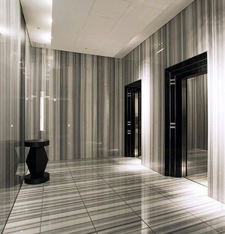 Modern elevator lobby featuring sleek striped walls, glossy floors, and a minimalist black side table.